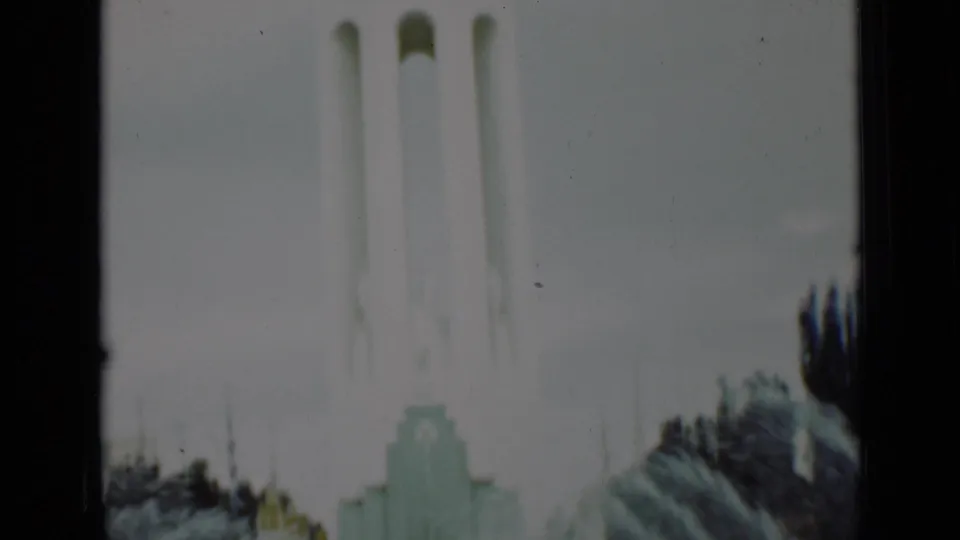 1937 San Francisco frame with a pale monument, trees, and a partially visible visitor at the edge of the home-movie shot.