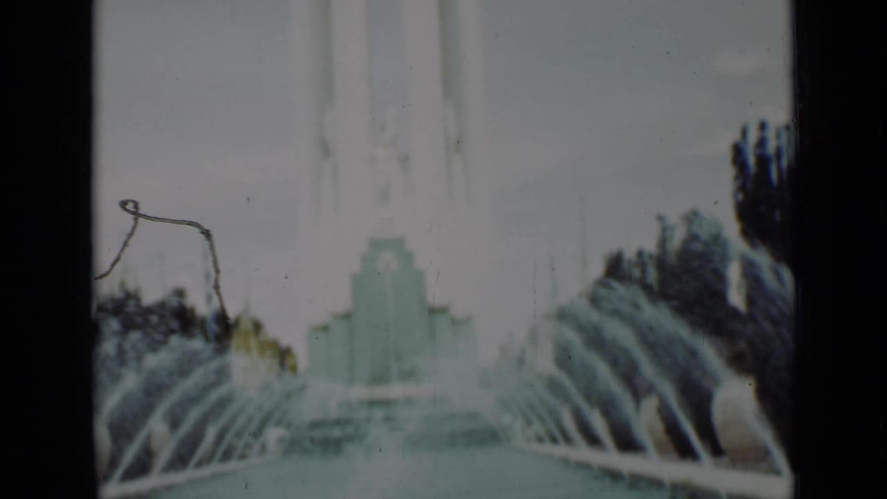 Fountain jets arc into a pool with a pale structure in the distance.