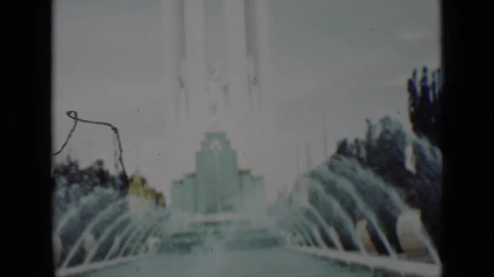 1937 San Francisco home-movie frame showing fountain jets, pool water, trees, and a pale architectural backdrop.