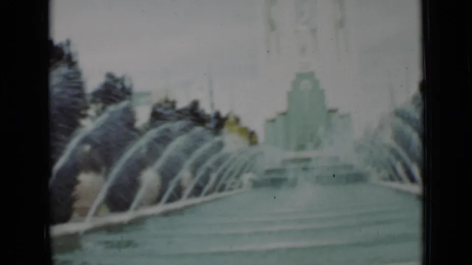 Soft 8mm frame of a 1937 San Francisco fountain, with repeated water arcs, pool edge, trees, and distant architecture.