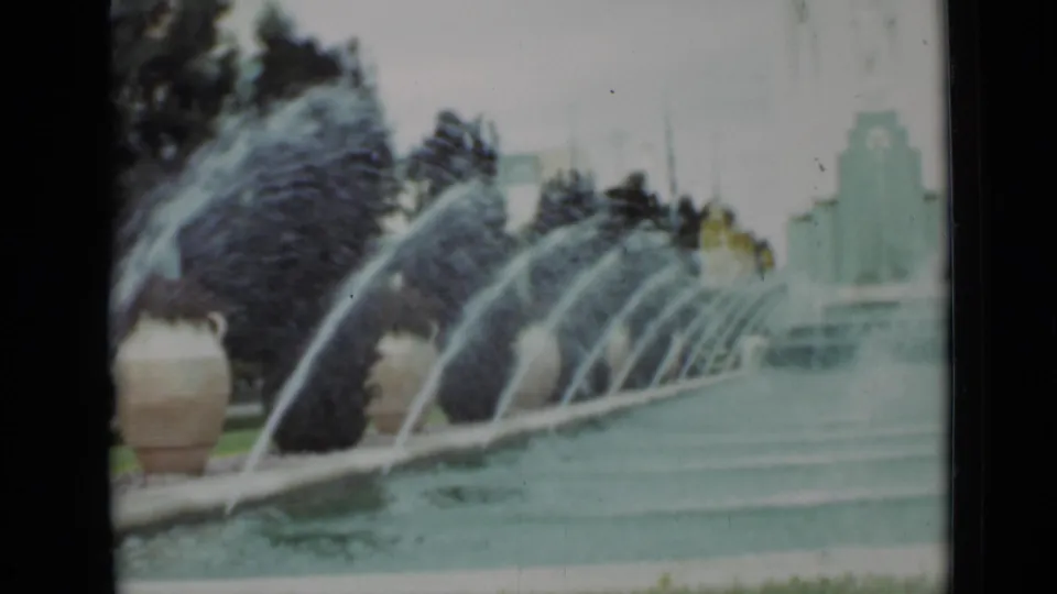 1937 San Francisco fountain scene with strong water arcs, pool water, dark trees, a planter, and pale architecture behind.