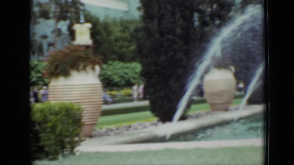 1937 San Francisco park footage showing fountain jets beside a large urn planter, hedges, trees, and distant park visitors.
