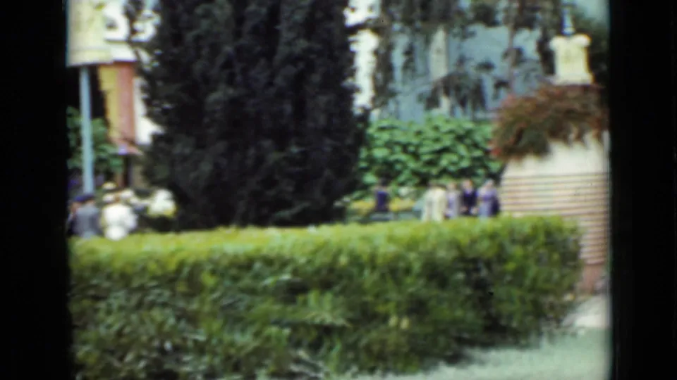 1937 San Francisco park scene with hedges, dark trees, a large urn planter, flower beds, and small groups of visitors.