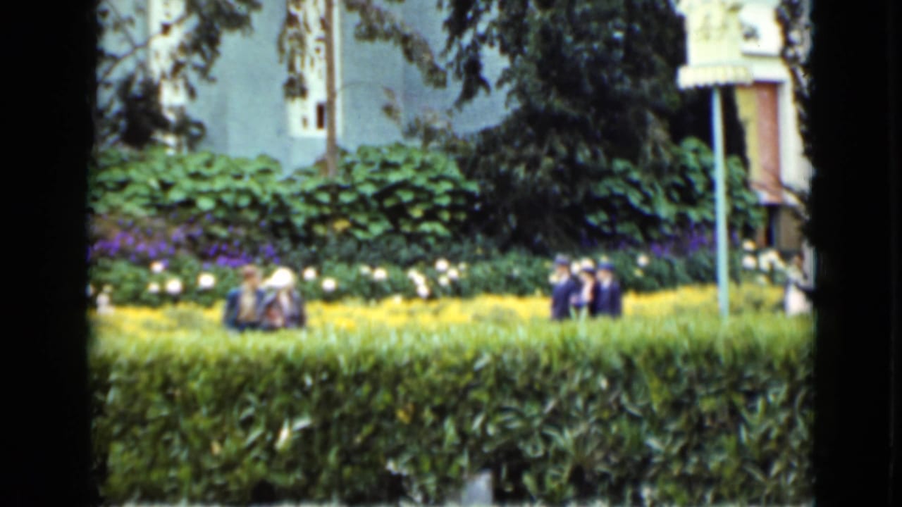 Visitors sit and walk near hedges and flower beds in a landscaped public park.