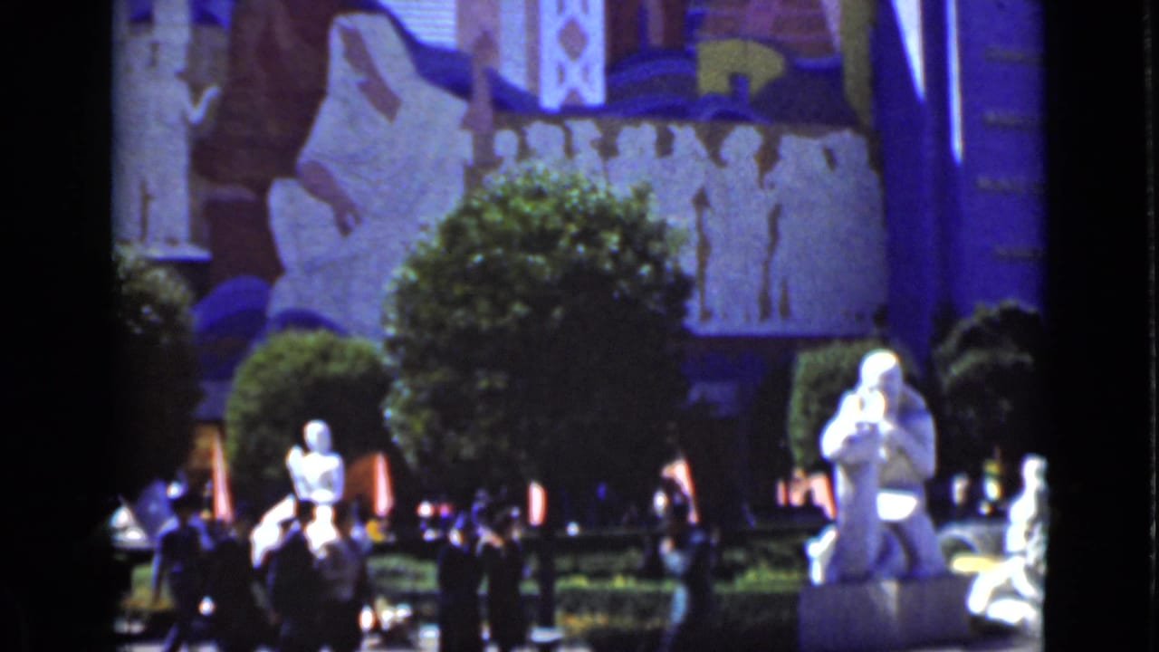 Visitors walk through landscaped grounds with white statues and a painted facade behind them.