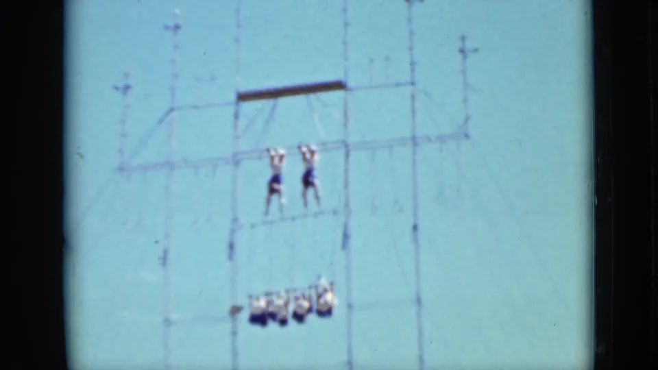 1937 San Francisco home-movie frame showing two acrobats suspended on a high rig with a small crowd or structure below.