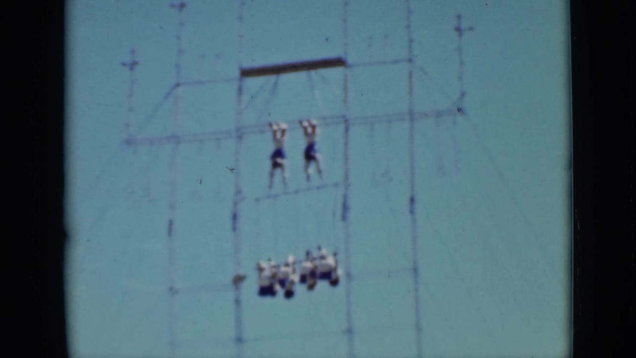 Two acrobats stand on high rigging above a lower hanging group.