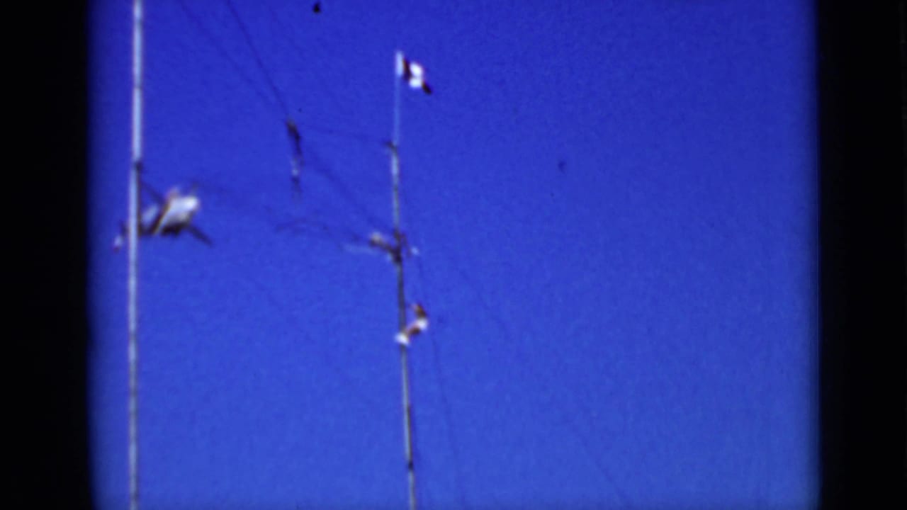 Blue sky with tall poles, a small flag, and a small airplane passing at left.