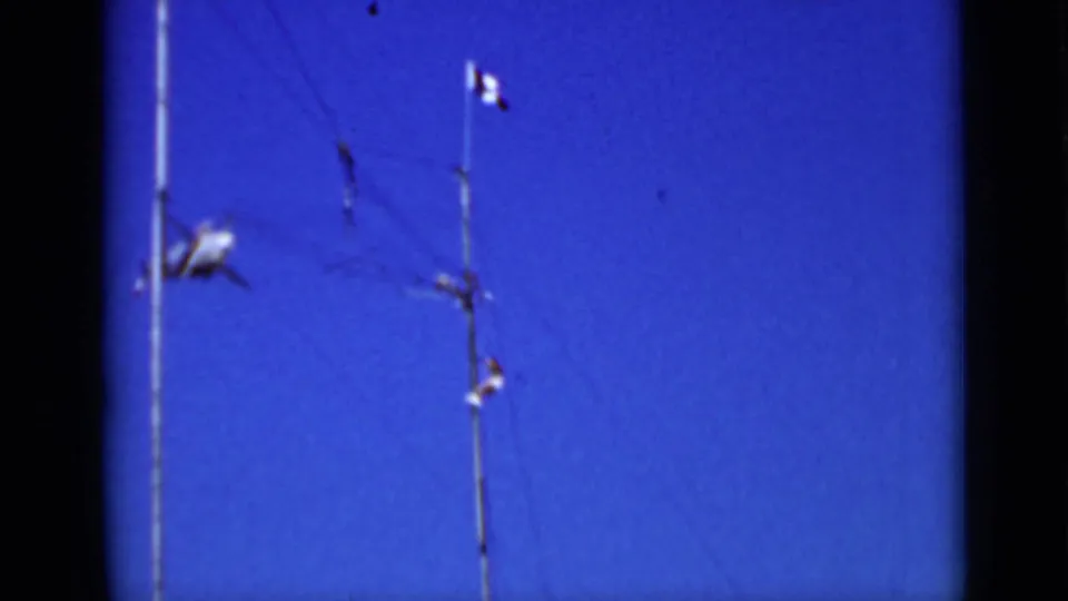 1937 San Francisco home-movie frame showing blue sky, tall pole structures, a French flag, and a small airplane in the distance.