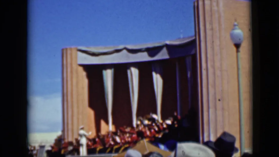 1937 San Francisco home-movie frame with a distant band on a bandshell stage and spectators gathered in front.
