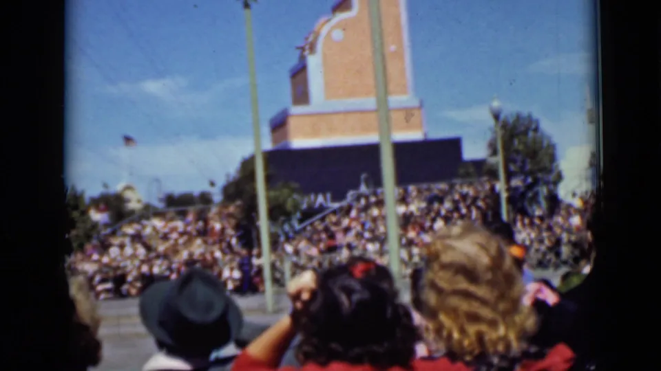 1937 San Francisco home-movie view of foreground spectators watching crowded bleachers beside a tall pole and brick tower-like backdrop.