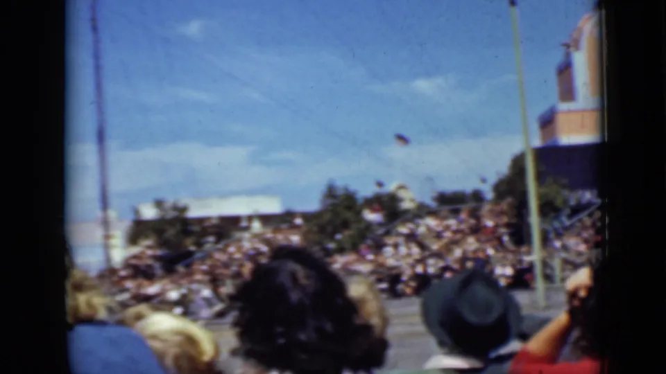 1937 San Francisco frame showing a crowded outdoor stand area with foreground heads, tall poles, and part of a brick tower-like structure.