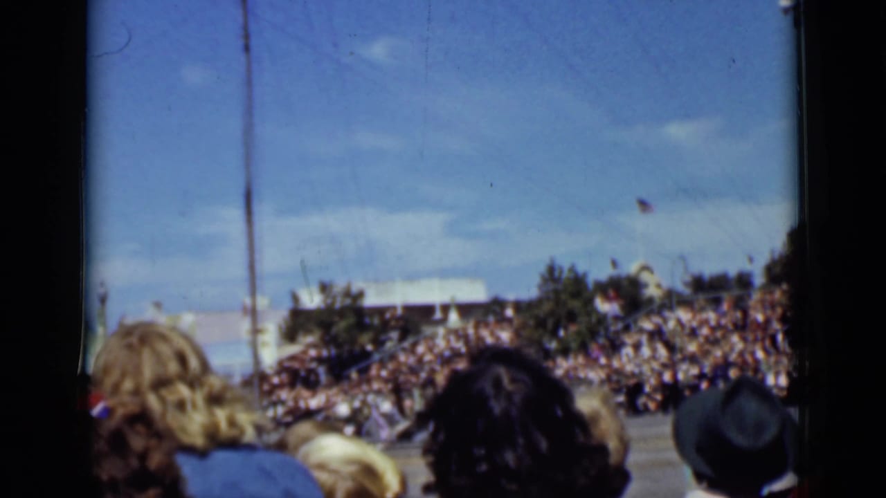 Crowd seen from behind watching an outdoor performance area under a blue sky.
