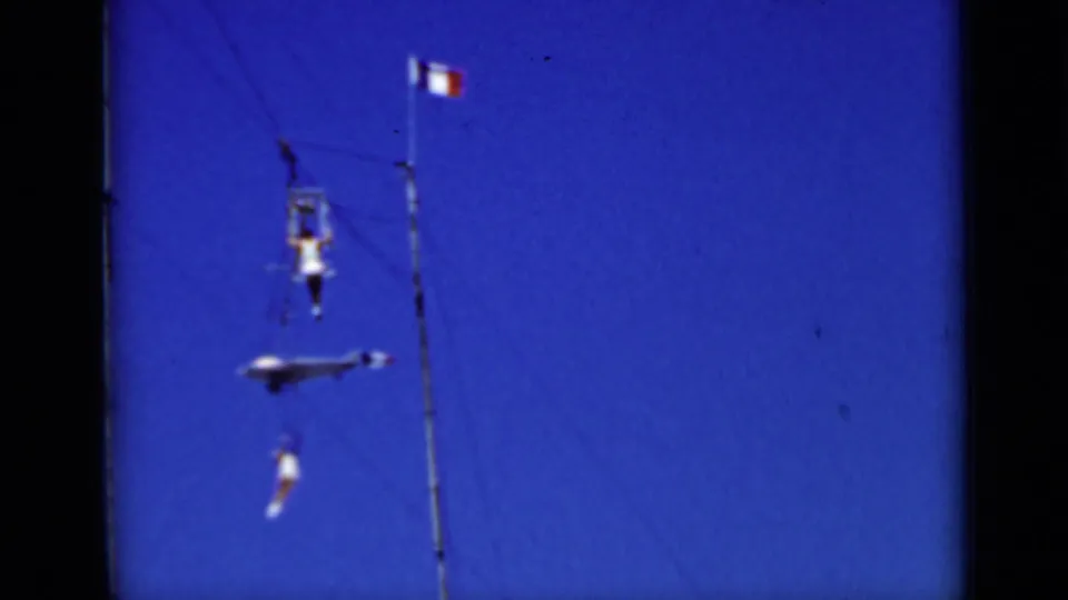1937 San Francisco frame showing trapeze performers suspended on rigging beneath a flag against a bright blue sky.