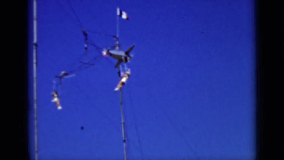 1937 San Francisco home-movie frame showing aerial performers on trapeze rigging high against a saturated blue sky.