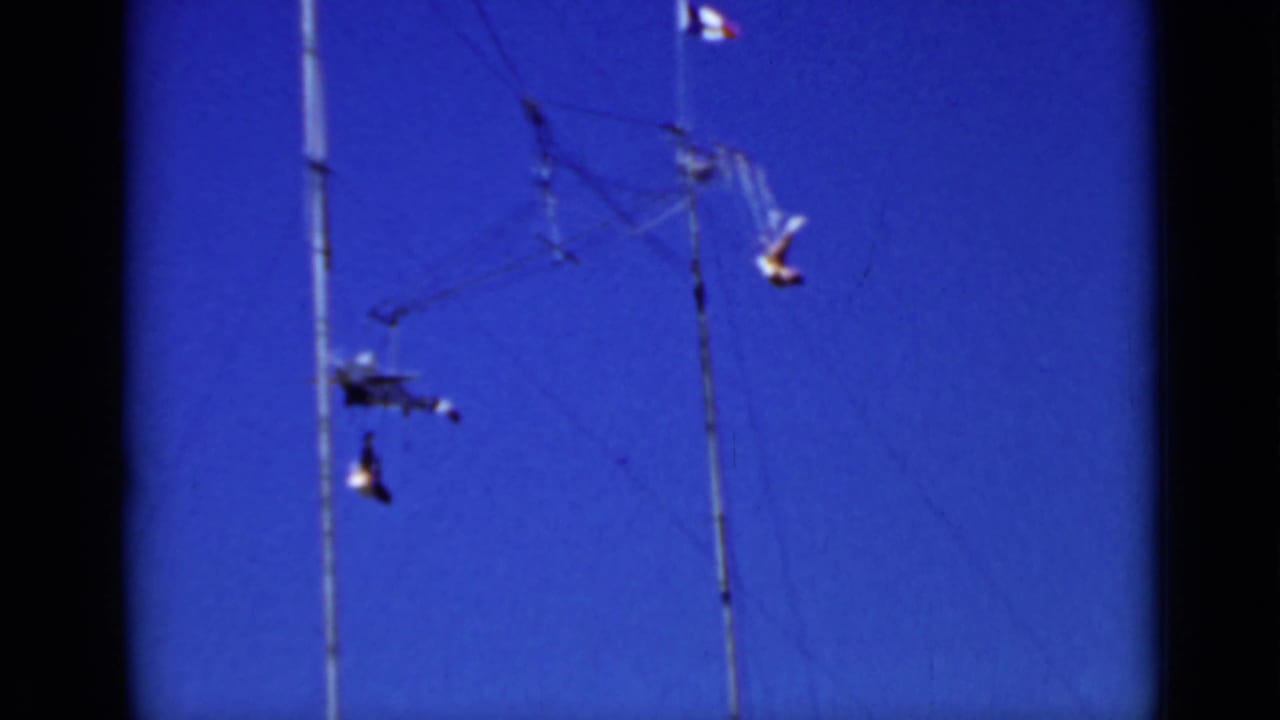 Small airplane mobile and dangling forms suspended from poles against a deep blue sky.