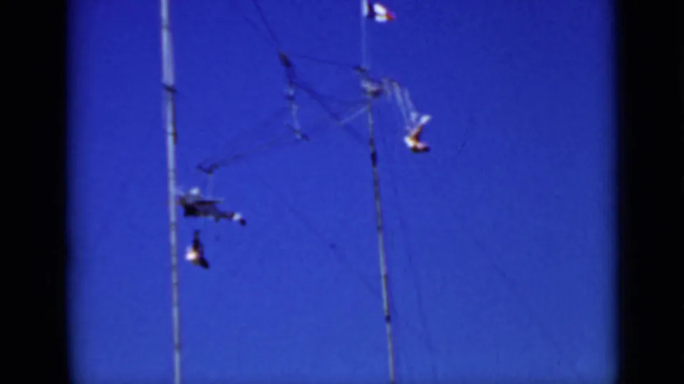 1937 San Francisco 8mm frame showing a small airplane-like mobile and dangling forms on tall poles against blue sky.