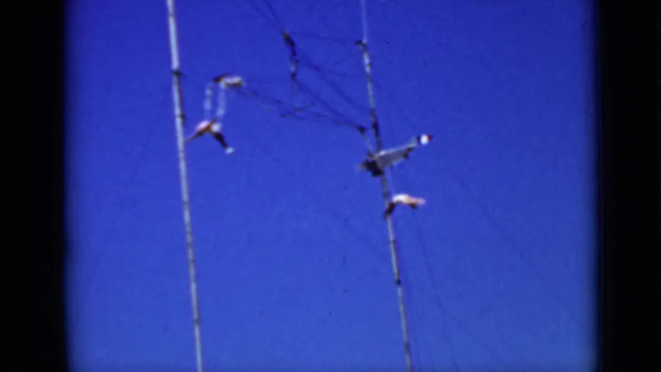 1937 San Francisco frame with a wire-suspended airplane-like mobile and tiny figure-like forms against saturated blue sky.