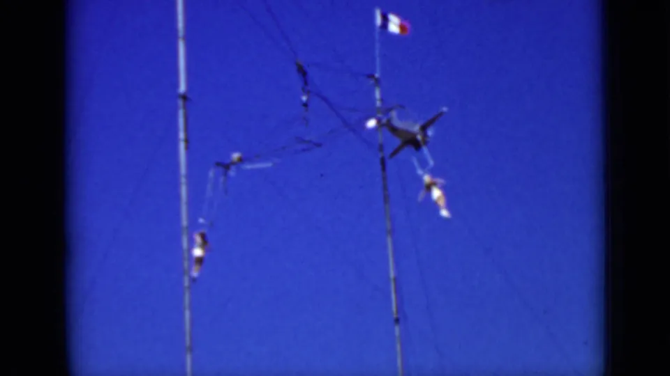 1937 San Francisco 8mm frame showing aerialists suspended on a tall outdoor rig beneath a small tricolor flag.