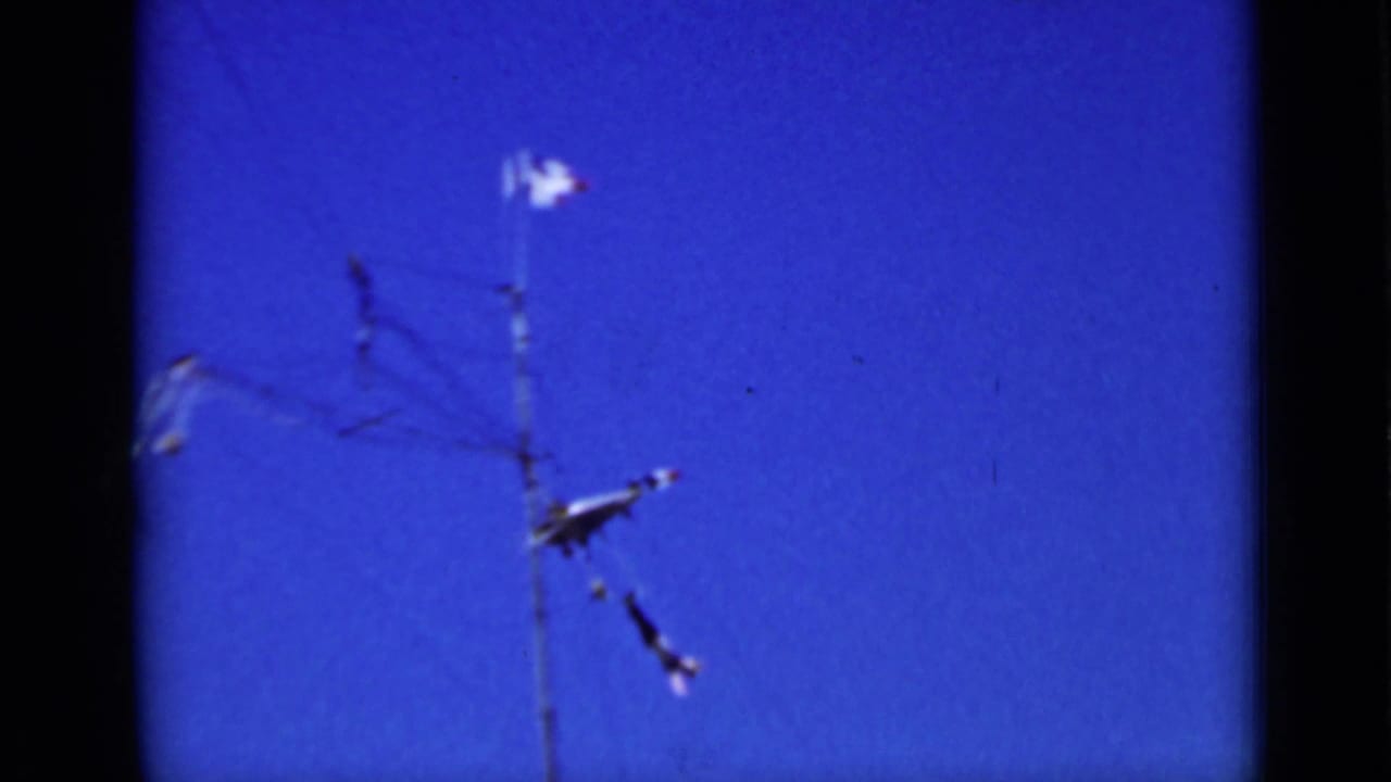 Metal toy airplane mobile near overhead wires against a clear blue sky.