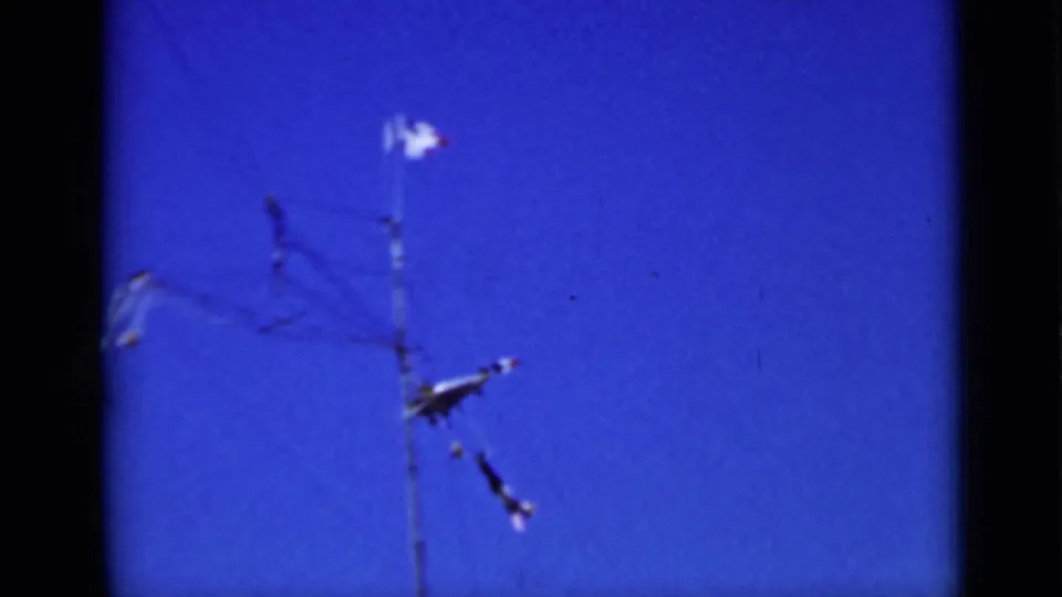 1937 San Francisco home-movie frame showing a small metal airplane mobile suspended near utility wires under a deep blue sky.