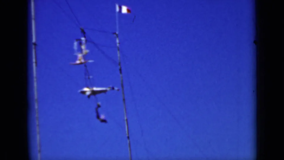 1937 San Francisco 8mm frame showing distant trapeze performers suspended high on rigging against a vivid blue sky.