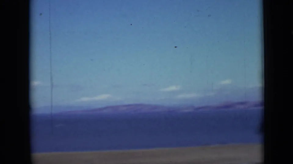 1937 San Francisco home-movie frame with distant landscape below the aerial rigging, including open ground and a blue horizon.
