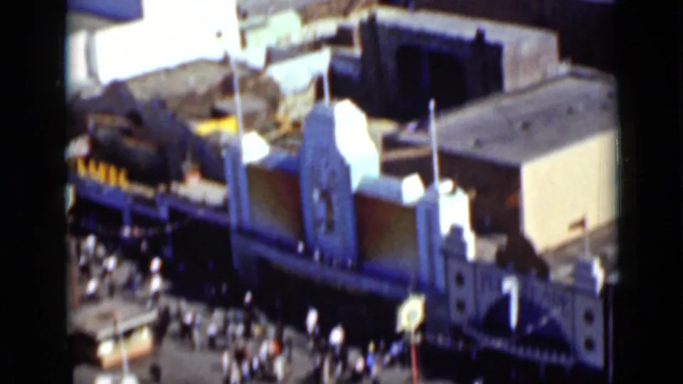 1937 San Francisco amusement-park frame showing a decorative building roofline, crowds below, and soft 8mm color blur.