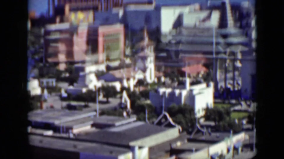 Wide 1937 San Francisco home-movie view with amusement buildings, ride structures, walkways, visitors, and surrounding rooftops.