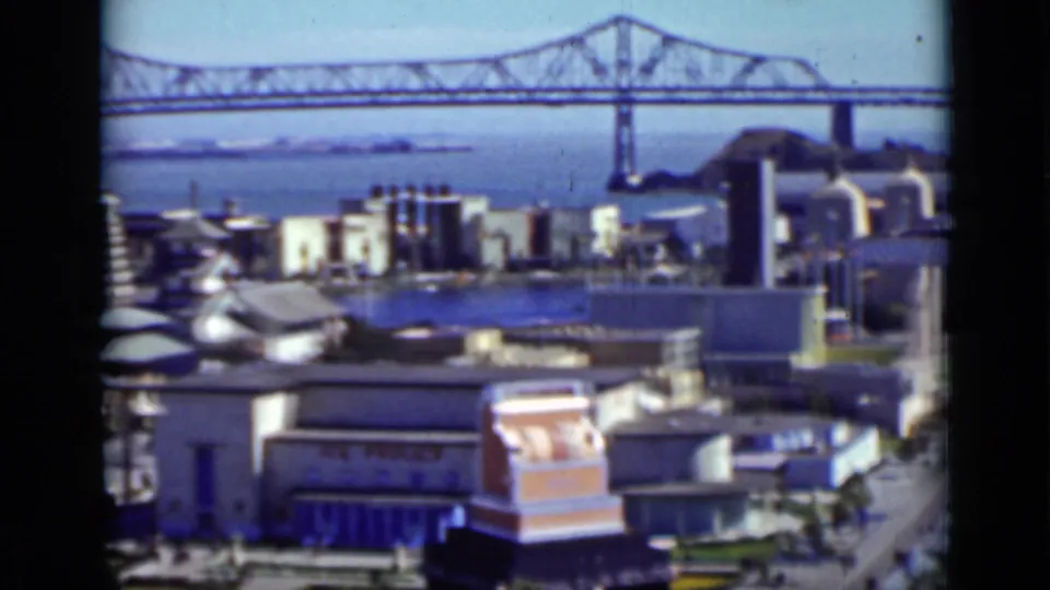 San Francisco waterfront buildings and bay water seen beneath a distant suspension bridge in this 1937 8mm frame.