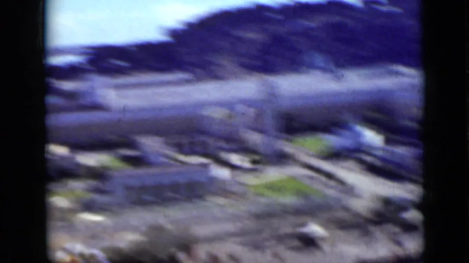 Motion-blurred 1937 San Francisco waterfront or shoreline view with low buildings, open ground, and a darker hillside beyond.