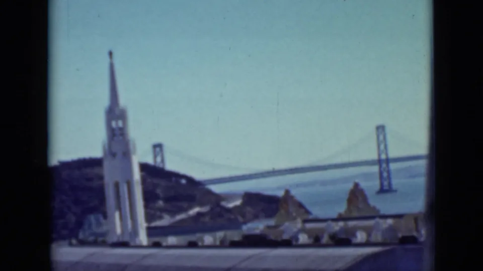 1937 San Francisco frame with a white tower, hillside, bay water, and bridge towers visible in the background.