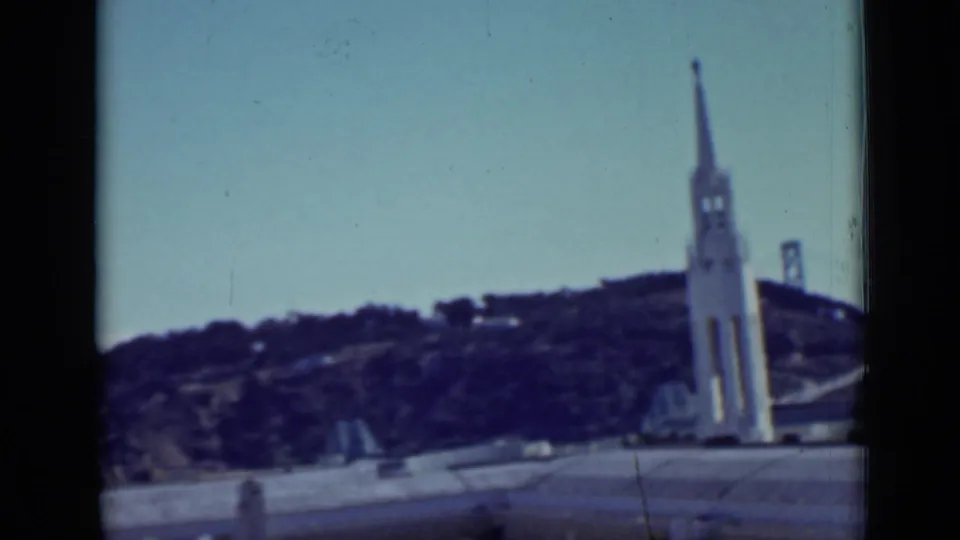 Final 1937 San Francisco frame showing a white tower, hillside streets, a partial bridge tower, road foreground, and blue sky.