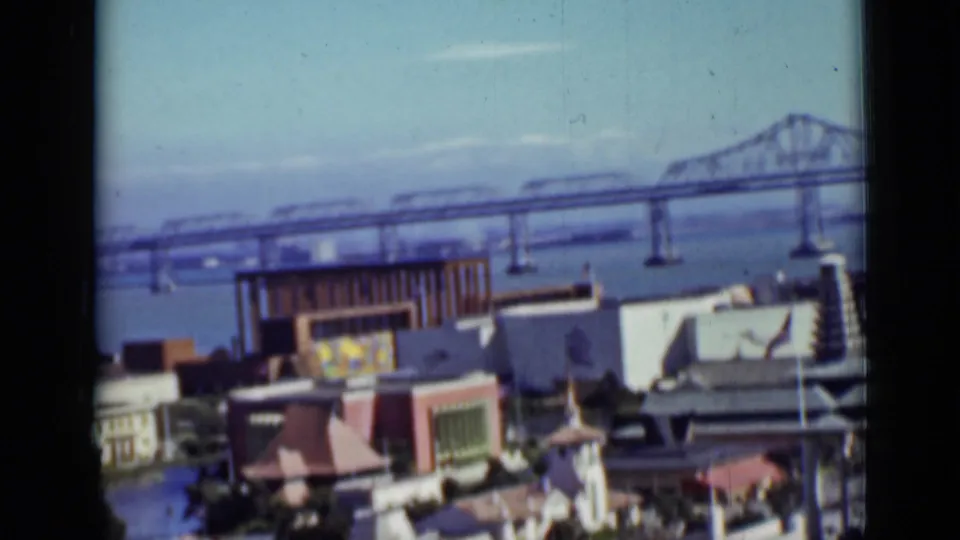 1937 San Francisco home-movie frame showing a wide bridge view over the bay with waterfront buildings below.