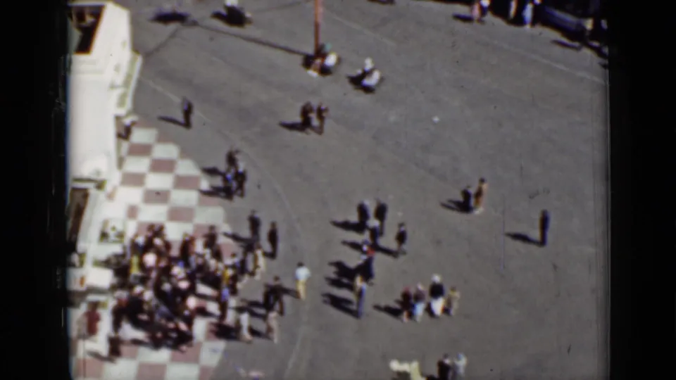 1937 San Francisco home-movie frame showing small groups of pedestrians on broad pavement beside a checkered tile corner.