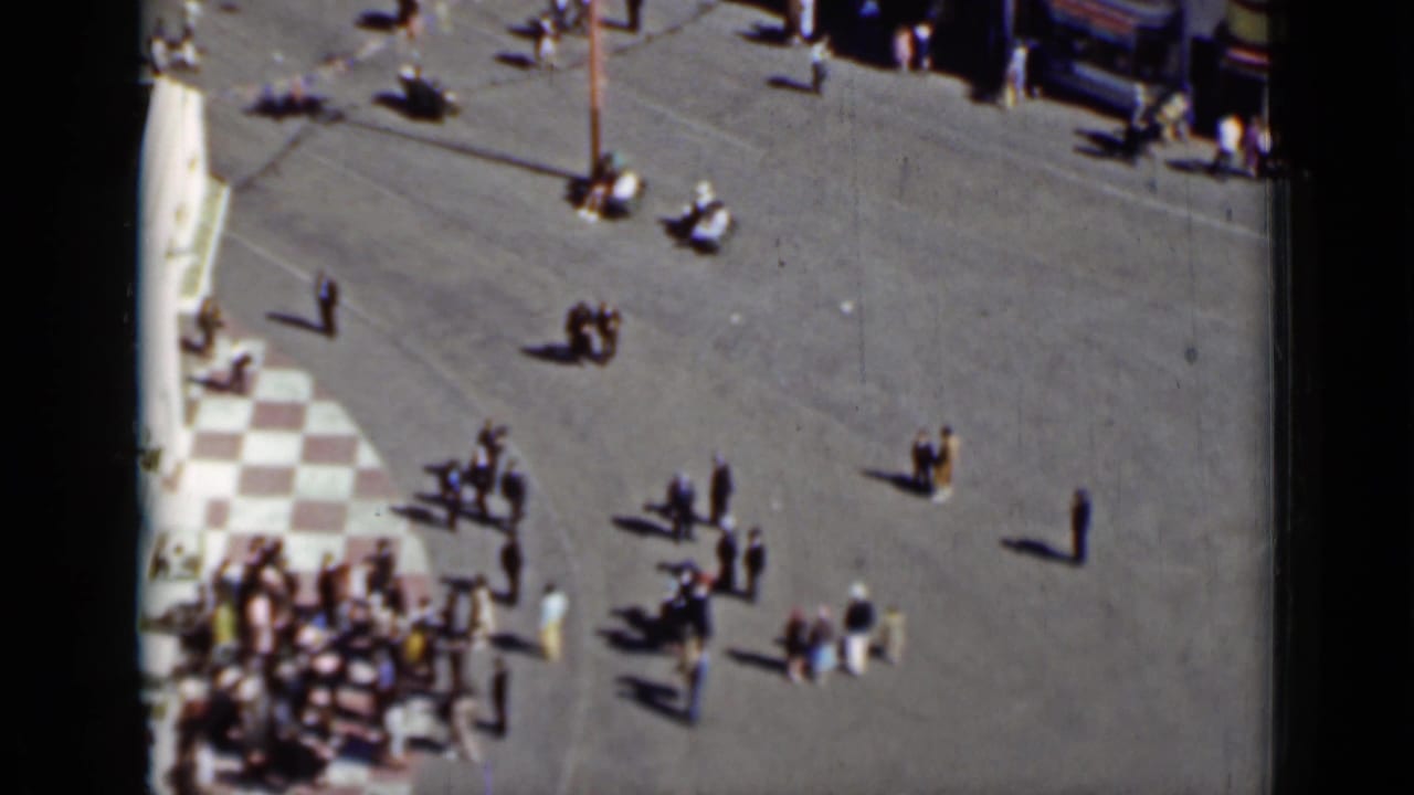 Distant pedestrians scattered across a broad paved area in bright sunlight.