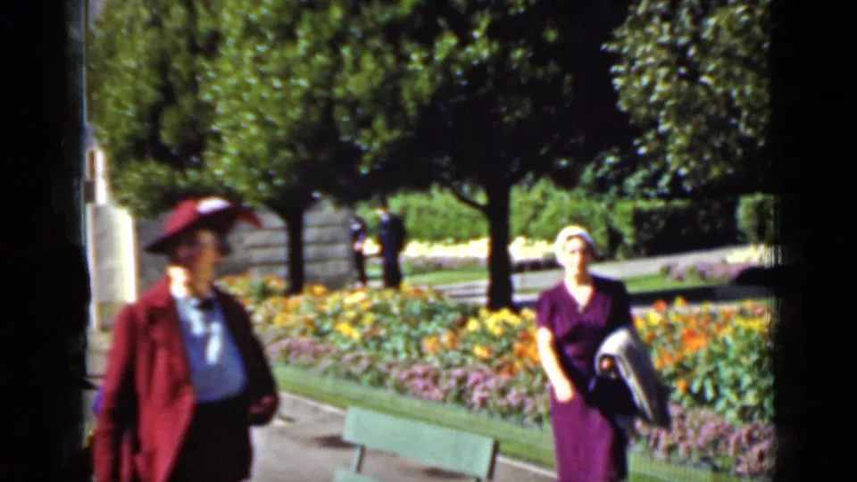 A second adult in a red jacket and hat enters the foreground as the woman in purple continues along the San Francisco garden path.