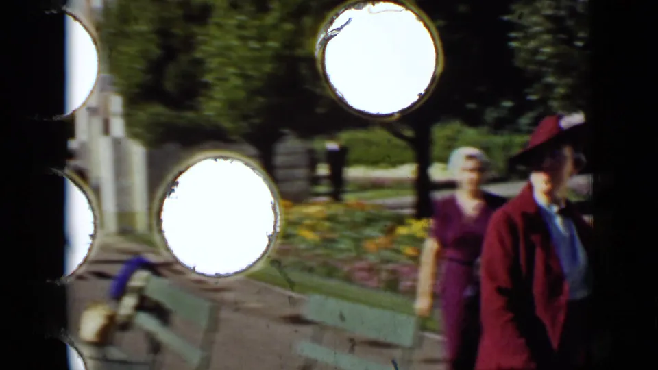 1937 San Francisco home-movie frame of two adult women in a landscaped park, partly obscured by large 8mm perforation flashes.