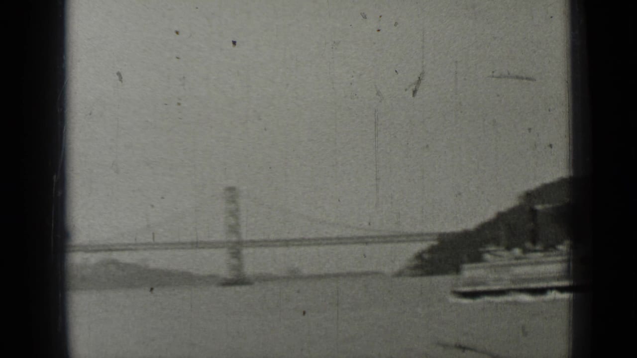 Bay Bridge span seen across water through dark vertical boat framing.