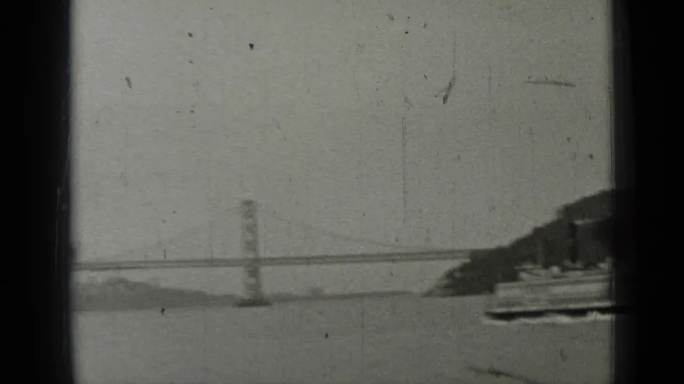 1937 8mm view across San Francisco Bay toward the Bay Bridge, framed by dark boat structure and soft film grain.