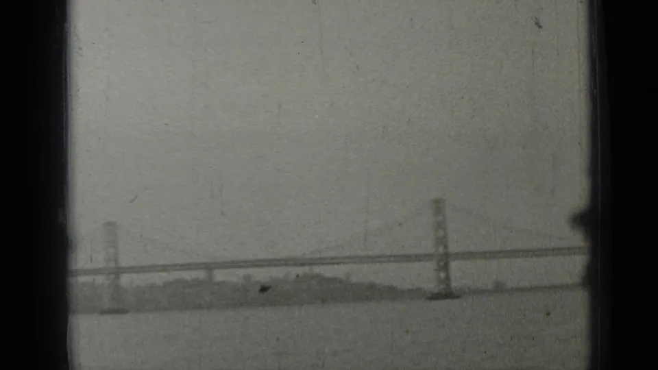 San Francisco Bay Bridge and shoreline seen from a moving boat, with another vessel partly crossing the frame.