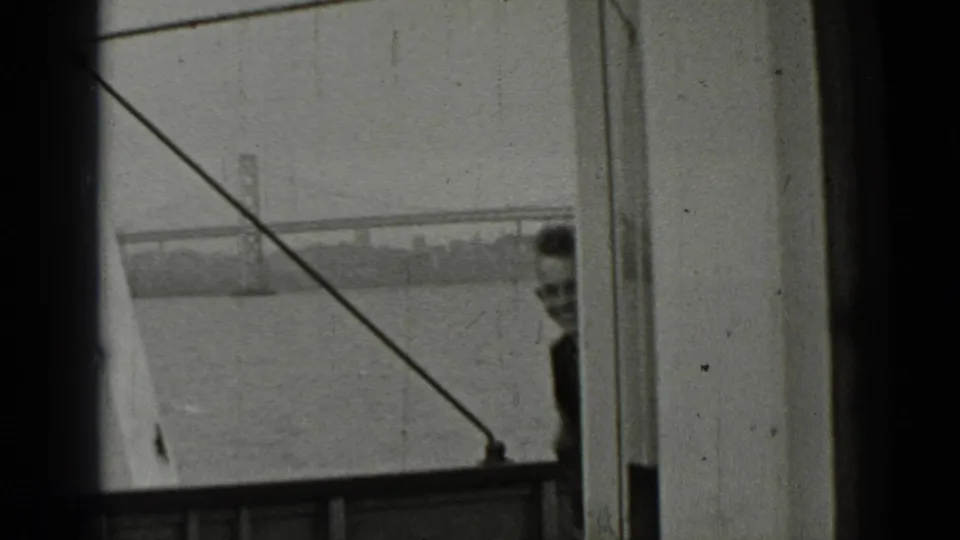1937 boat-side view of the Bay Bridge, with rigging crossing the frame and a partially visible person near the right edge.