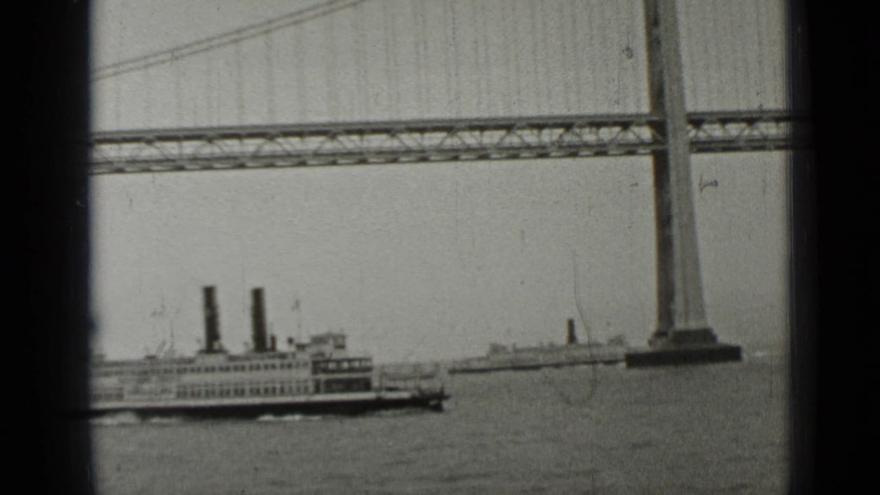 Ferry with twin smokestacks moving on bay water beneath a suspension bridge.
