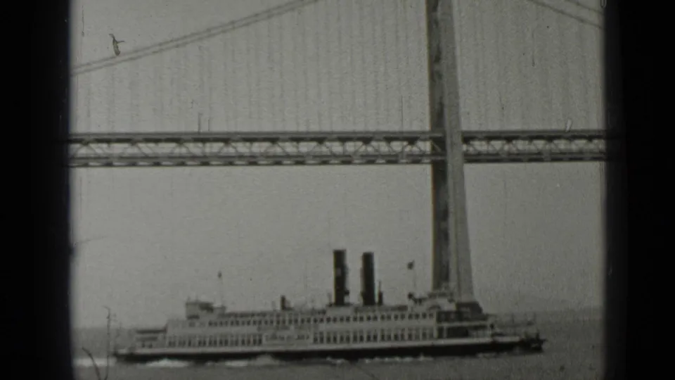 1937 San Francisco home-movie frame showing a steamship or ferry moving under a large suspension bridge.