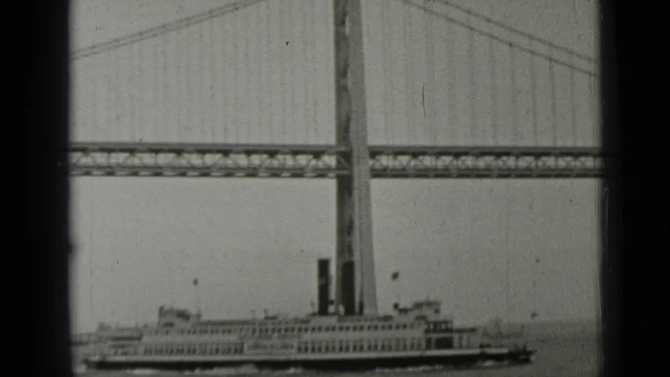 1937 San Francisco frame of a steamship or ferry crossing the water below a suspension bridge span.