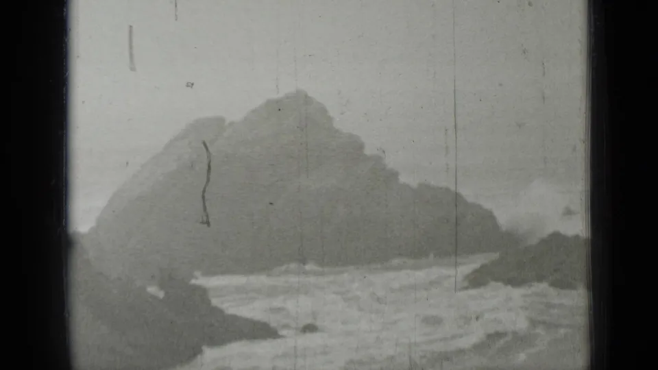 Black-and-white 1937 California coastal view with waves breaking against rocks below hazy cliffs.