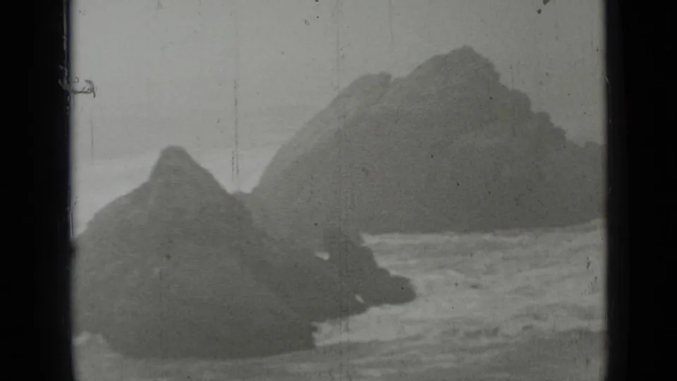 1937 San Francisco-area 8mm frame showing dark coastal rocks, rough surf, mist, and visible film scratches.