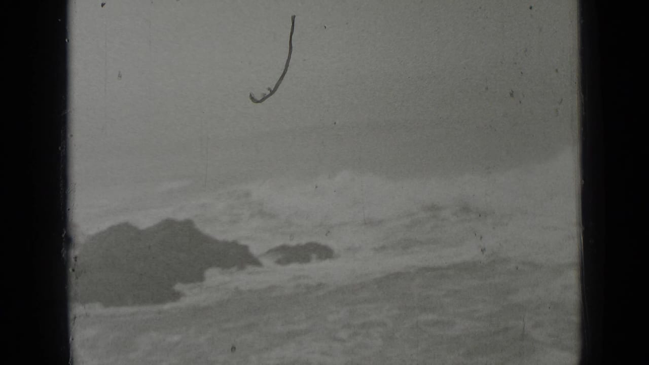 Dark rocks and turbulent waves beneath an overcast sky.