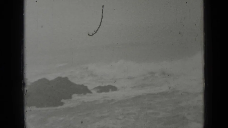 1937 San Francisco coastal home-movie frame showing dark offshore rocks and rough surf under a gray sky.