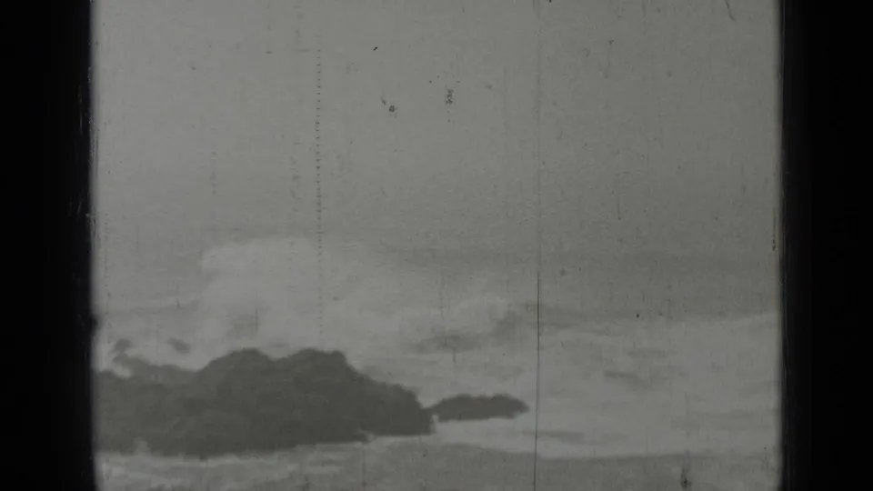 1937 black-and-white 8mm view of rocky Pacific shoreline near San Francisco with surf rolling in beneath an overcast sky.